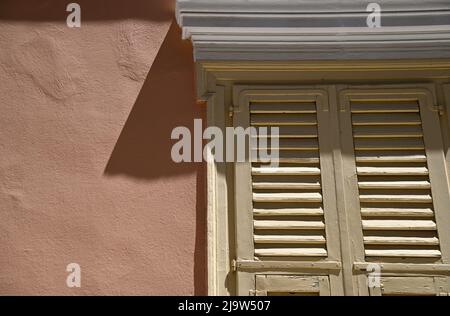 Old Neoclassical house mellow ochre wooden window louvered shutters with a white plaster head on a salmon pink Venetian stucco wall. Stock Photo