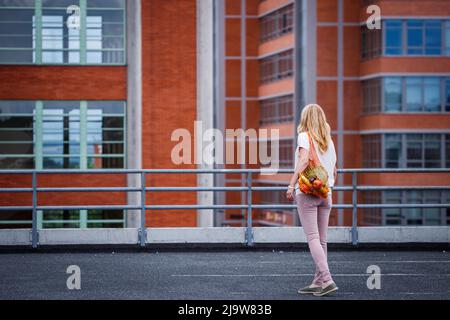 Woman walking with reusable mesh bag full of fruits. Sustainable lifestyle, plastic free shopping and zero waste concept Stock Photo