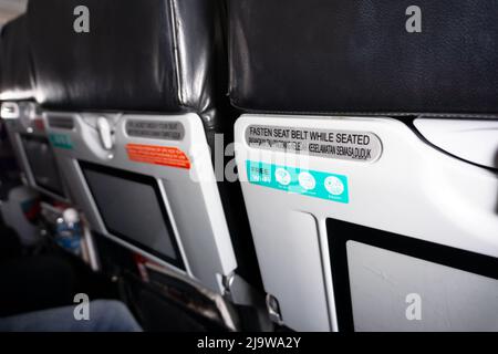 Seat belt safety sign on a commercial aircraft - Fasten seat belt while seated advice at the back of commercial airplane seat Stock Photo