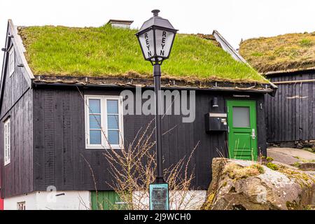 Tummasarstova, a turf-roofed, black-painted timber house with a green door, stands on the lane Reyn in the old town of Tórshavn, the capital of the Faroe Islands, with a historic street lamp labelled "Reyn" standing in front. Named houses like this are common throughout Tórshavn's historic old town. Stock Photo
