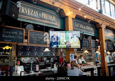 As pictures of Spain's former king Juan Carlos in exile in Abu Dhabi are broascast on national TV, customers enjoy afternoon drinks at La Casa del Indiano, a bar and restaurant in the covered Mercado del Este, on 19th May 2022, in Santander, Cantabria, Spain. King Juan Carlos Felipe VI has been in exile in the Gulf state after being accused of money-laundering but the case was closed due to lack of evidence. Mercado del Este was designed by architect Antonio Zabaleta. Construction was between 1839 and 1842 and is considered to be one of the first examples of market 'galleries' built in Spain. Stock Photo