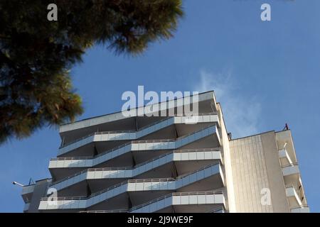 Facade of a european beautiful high hotel with open terraces, in resort area on sea, against background of sky blue Stock Photo
