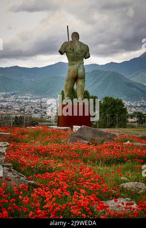 Statue of Daedalus by Igor Mitoraj in the UNESCO World Heritage Site of Pompeii. Daedalus surrounded by poppies looks out over the city of Pompeii and Stock Photo