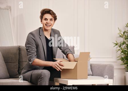 man sitting on the couch and unpacking cardboard box. Stock Photo