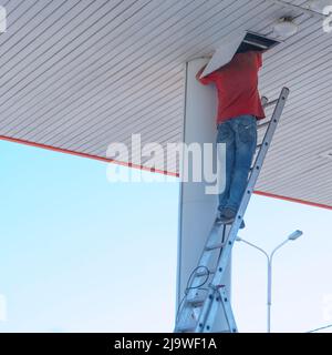 A worker on a stepladder checks or repairs something in a hatch on the ceiling Stock Photo