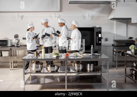 Team of multiracial cooks having conversation during a coffee break in the kitchen. Well-dressed chefs resting and having fun in the restaurant kitchen. Teamwork and leisure time on work Stock Photo