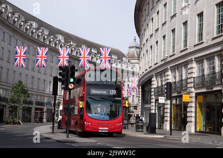 A red London bus goes under the Union Jacks on Regent Street in London. Bunting/flags are up ready for the Queens Platinum Jubilee, taken 21st May 202 Stock Photo