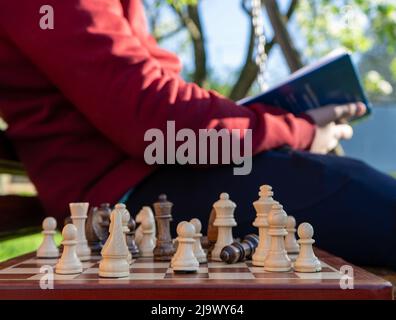 Wooden chess, a chess player is studying in the background, reading a book. Education concept, intellectual game, training, tournament Stock Photo