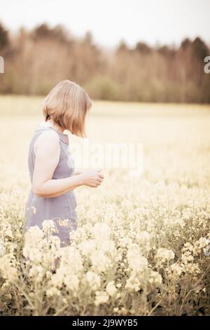 Concept Mindfulness;  Womens health; A middle aged caucasian woman  standing in a field of flowers in spring, in profile, high key image, Suffolk UK Stock Photo