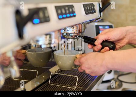 Close-up of professional barista holding cup and preparing coffee in a carob coffee machine in cafe Stock Photo