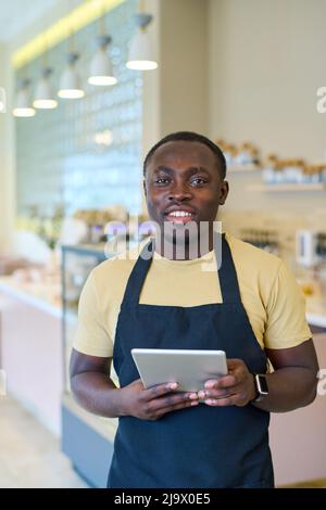Portrait of African smiling cafe owner in apron using digital tablet at work Stock Photo