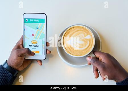 Close-up of African man booking taxi online using application on smartphone while drinking coffee Stock Photo