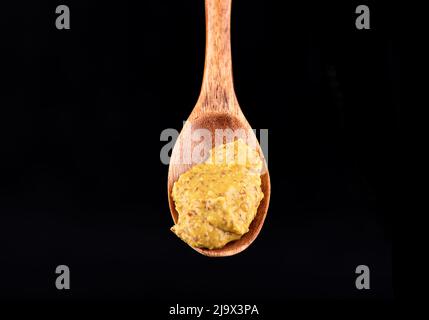 Close-up of a wooden spoon with french mustard on a black background. Copy space. Stock Photo