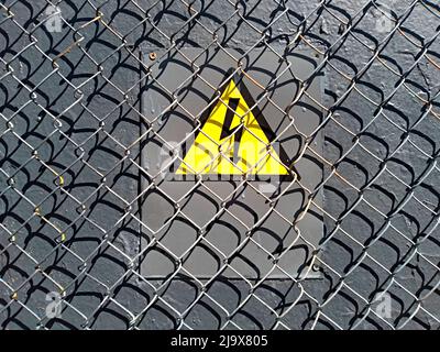 electrical hazard sign placed on an electric power substation behind a metal fence of wire mesh, sanctions, restrictions Stock Photo