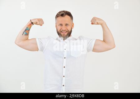 Bearded attractive, powerful, smiling man in white outfit on white background. Showing and proud relief muscles on arms Stock Photo