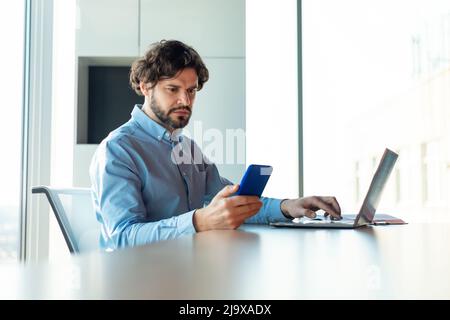 Portrait of focusedman using smartphone and pc at office Stock Photo