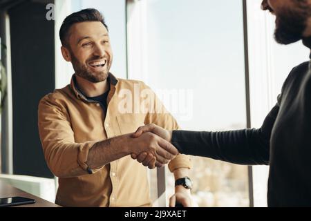 Business partnership. Two happy businessmen handshaking after successful deal at modern office Stock Photo