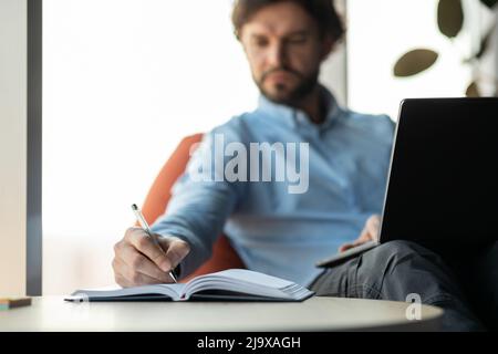 Close up of man using laptop and writing in notebook Stock Photo