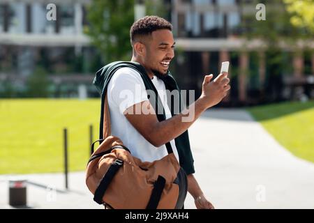 Smiling black man using phone walking in the city Stock Photo