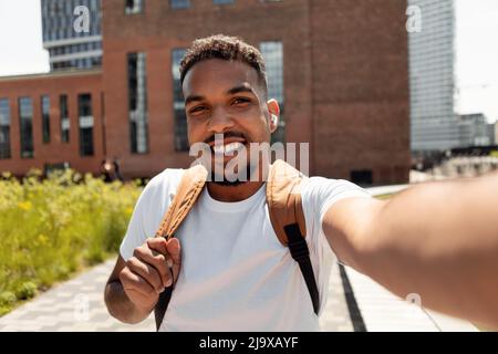 Happy young man taking selfie picture in earbuds walking outdoors Stock Photo