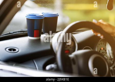 two blue paper coffee cups on car dashboard. Paper Cup with hot tea. young Woman driving. cropped photo. High quality photo. Stock Photo