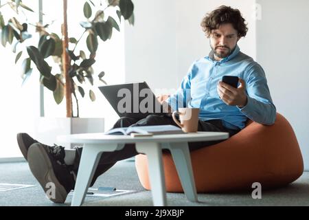 Portrait of focused man using smartphone and pc at office Stock Photo