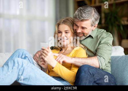 Happy Middle Aged Couple Relaxing With Smartphone On Couch At Home Stock Photo
