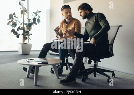 Serious male colleagues communicating at company office, using tablet pc, discussing common business project Stock Photo