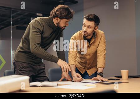 Male colleagues working on startup project together, writing down info, having discussion at modern office Stock Photo