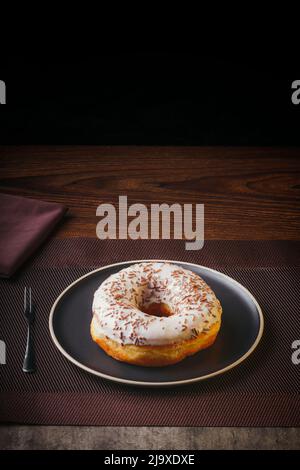 Tasty donut isolated on a plate on a fine table. Donuts, with white chocolate sprinkled with chocolate chips, Fine pastries Stock Photo