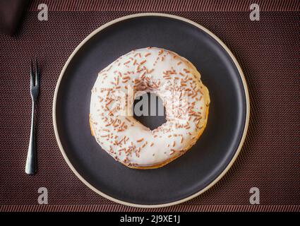 Tasty donut isolated on a plate on a fine table. Donuts, with white chocolate sprinkled with chocolate chips, Fine pastries Stock Photo