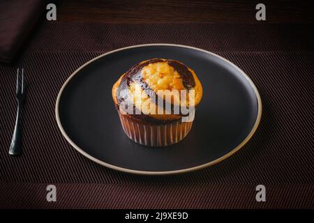 Vanilla Muffin with chocolate marbled on brown paper isolated on a thin plate on a nice table, fine pastries Stock Photo