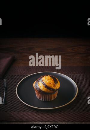 Vanilla Muffin with chocolate marbled on brown paper isolated on a thin plate on a nice table, fine pastries, Copy space Stock Photo