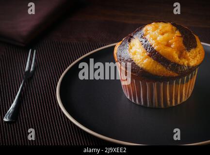 Vanilla Muffin with chocolate marbled on brown paper isolated on a thin plate on a nice table, fine pastries, close-up Stock Photo