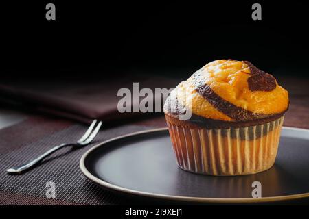 Vanilla Muffin with chocolate marbled on brown paper isolated on a thin plate on a nice table, fine pastries, close-up Stock Photo