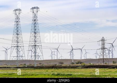 High voltage electricity towers and lines crossing the Sacramento-San Joaquin Delta; Wind turbines visible on the hills in the background; Solano Coun Stock Photo