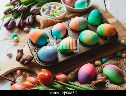 Tray of brightly colored easter eggs surrounded by tulips. Stock Photo