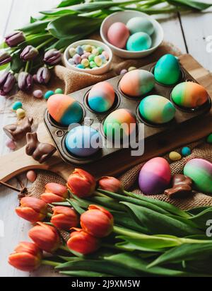 Tray of brightly colored easter eggs surrounded by tulips. Stock Photo