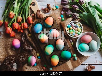 Tray of brightly colored easter eggs surrounded by tulips. Stock Photo