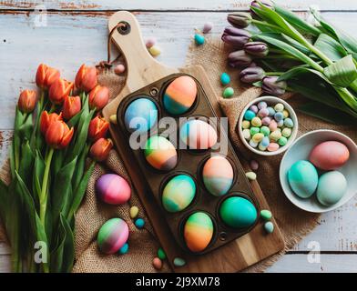 Tray of brightly colored easter eggs surrounded by tulips. Stock Photo