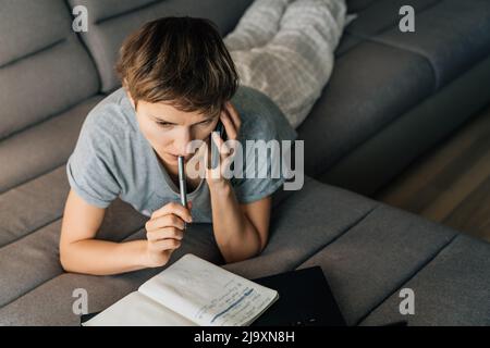 Woman takes notes while talking on her cell phone in her home clothes Stock Photo