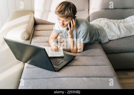 Woman lies on couch, talking on the phone and taking notes Stock Photo
