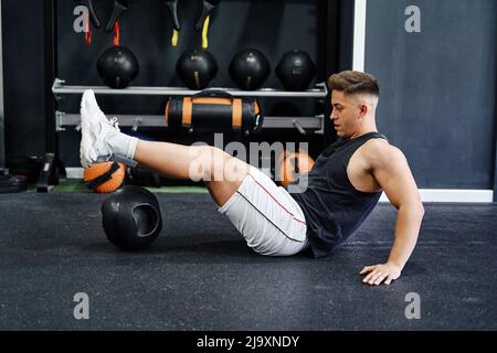 man doing strengthening exercise with ball on mat in gym Stock Photo
