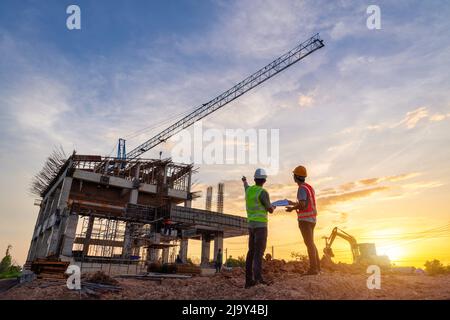 Architect civil Engineer and worker checking project at building site background, construction site at sunset in evening time. Silhouette of construct Stock Photo