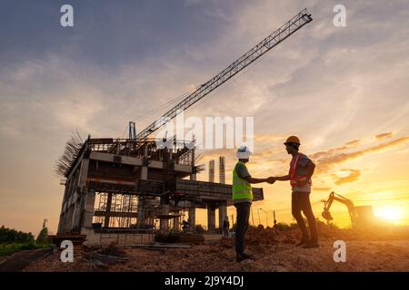Architect civil and engineer in protective helmets and vests are shaking hands while working in construction site. Stock Photo