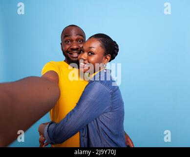 POV ofcheerful lovers in relationship in front of camera, taking pictures together in studio. Cheerful couple using phone in hand to take selfies and share romance. Partners hugging each other Stock Photo