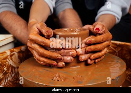 dirty hands close up . romantic couple in love working together on potter wheel and sculpting clay pot,a bearded man and a young woman mold a vase in Stock Photo