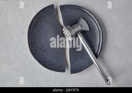 Broken ceramic plate and a kitchen hammer on a light concrete table Stock Photo