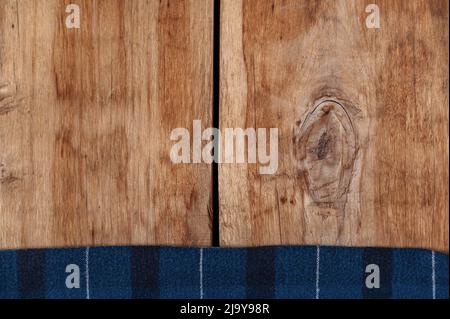 The blue checkered fabric lies against the wooden background. A towel or kitchen napkin on the rough boards or kitchen table. Stock Photo