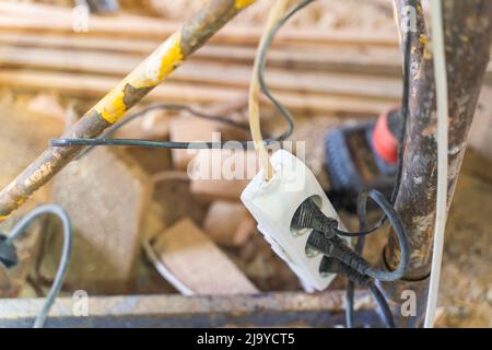 Power filter extension cord tee with euro sockets hanging on scaffolding with three connected electrical appliances, close-up Stock Photo